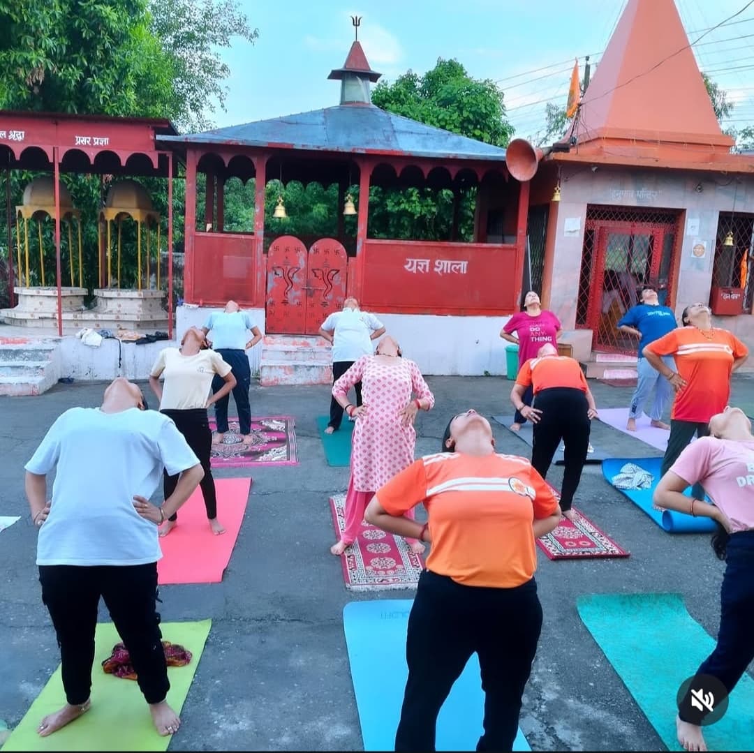 Outdoor group yoga class with students in a standing backbend pose in front of a temple courtyard